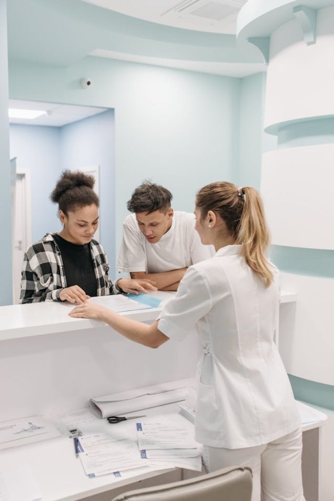 A nurse assists two patients at a hospital reception, emphasizing healthcare service.